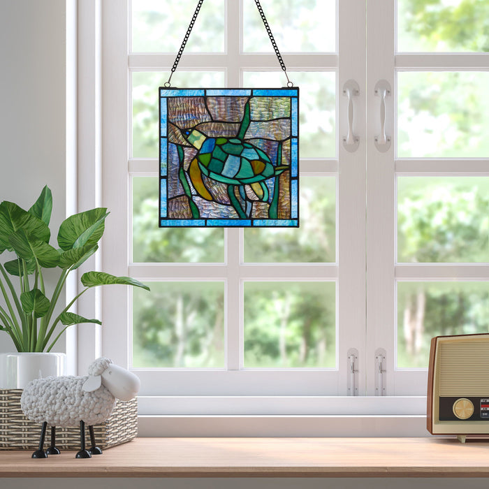 10.5"H Tommy the Green Sea Turtle Stained Glass Window Panel
 on a windowsill with a view of trees outside.