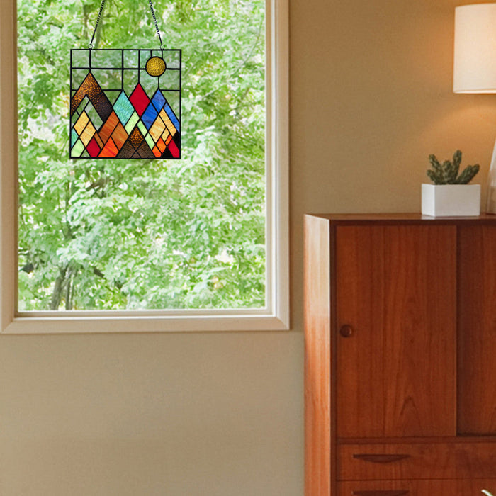 10"H Beyond the Mountain Tops Multicolored Window Panel hanging on a window with a wooden cabinet and plant in the background.
