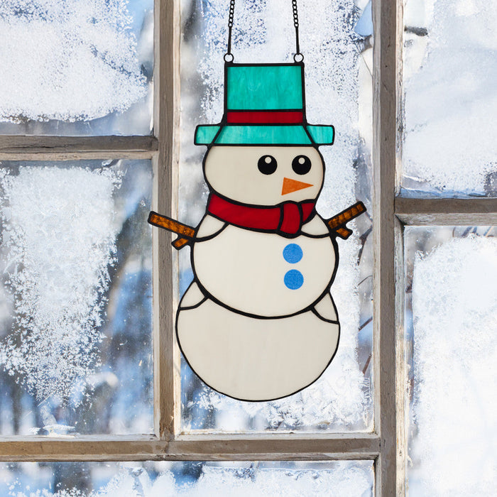12" H Tiffany-Style Spirited Holiday Snowman Stained Glass Window Panel hanging on a window with a snowy background