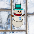 12" H Tiffany-Style Spirited Holiday Snowman Stained Glass Window Panel hanging on a window with a snowy background