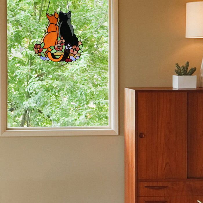 12.5"H Stained Glass Cats in the Garden Window Panel hanging by a window with greenery outside.