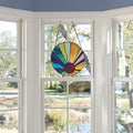 12.75"H Serenity Stained Glass Window Panel hanging in a window with a view of trees and sky.