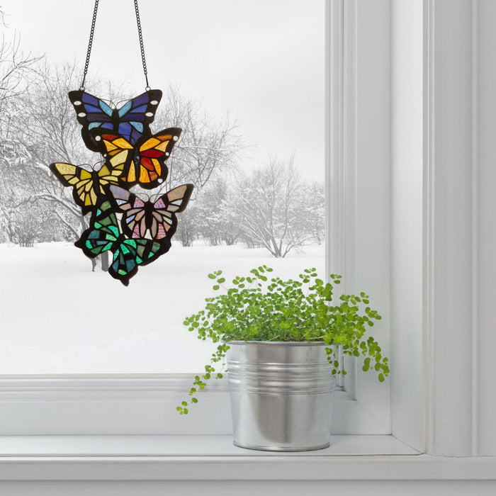 13.25" H Butterfly Cluster Stained Glass Window Panel hanging on a snowy window with a plant below