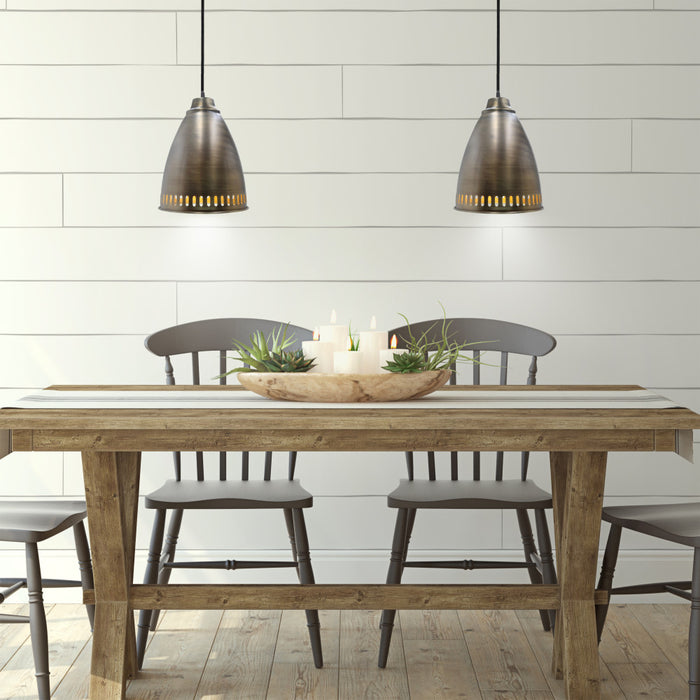 13"H Pierced Brushed Metal Cone 1-Light Pendant in a dining room with wooden table and chairs against a white paneled wall.