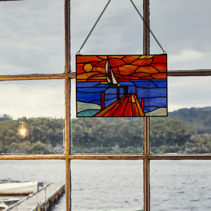 14" L Sailboat Stained Glass Window Panel hanging in front of a window with a view of water and trees.