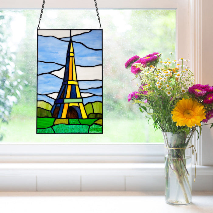 14.5" H Eiffel Tower Stained Glass Window Panel hanging in a window with a vase of flowers beside it.