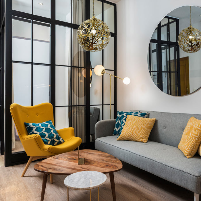 16" W Jillian Industrial Abstract Gold Metal Globe Shade Pendant Light in a modern living room with yellow chair, gray sofa, and wooden coffee table.
