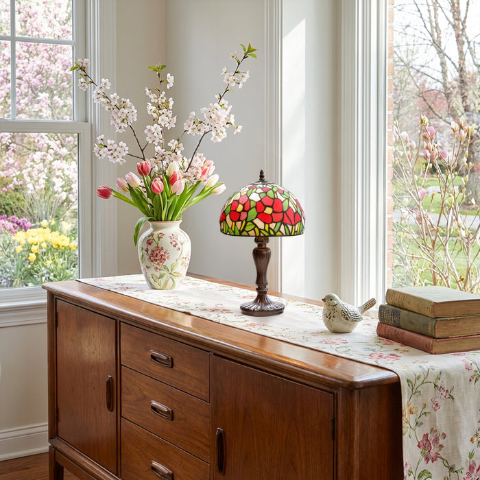 17" H Genevieve Red Flowers Stained Glass Candlestick Table Lamp in a wooden sideboard with floral arrangement, and books in a bright room with windows.