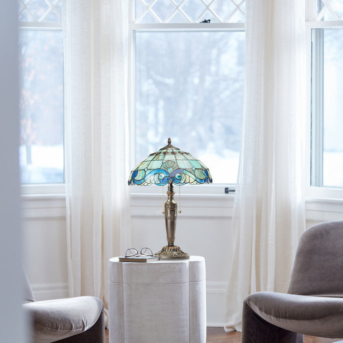 20"H Vivienne Baroque Style Stained Glass Table Lamp on a small table in a room with large windows and white curtains.