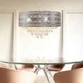 24"W Brielle Polished Nickel and Crystal 3-Light Chandelier hanging above a glass dining table with chairs in a room.