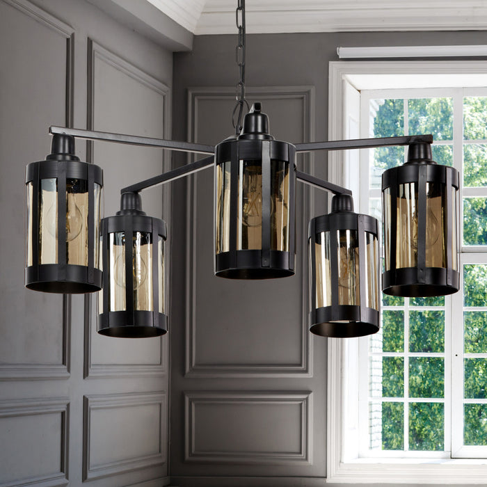 25" W 5-Light Marcell Metal and Glass Chandelier in a room with gray walls and a window.