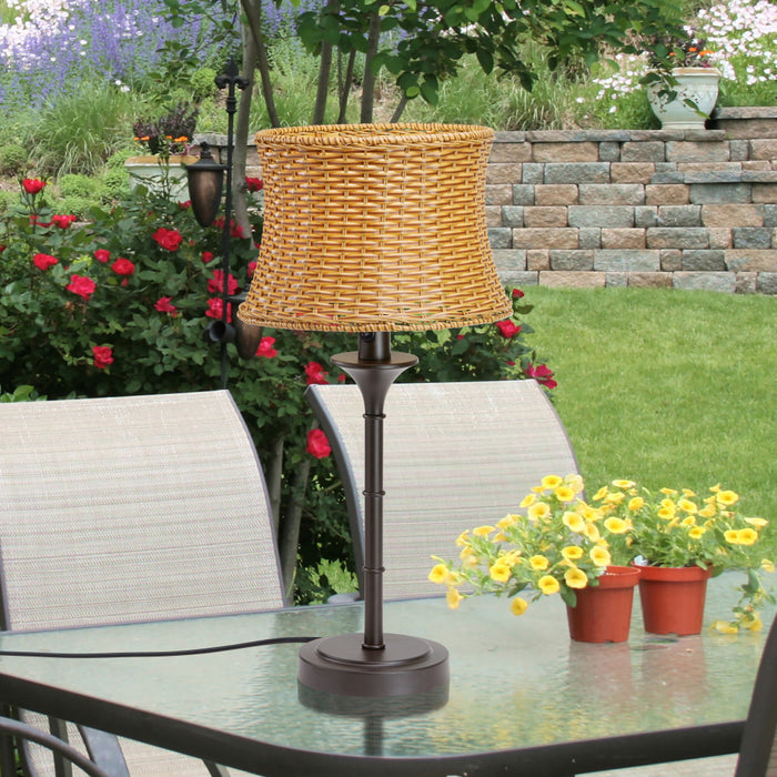 25.25"H Outdoor and Indoor Basket Weave Table Lamp on a glass patio table with flowers and chairs in the background