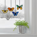 3.2" H Butterfly Kaleidoscope Stained Glass Window Panel Set hanging above a potted plant on a windowsill.