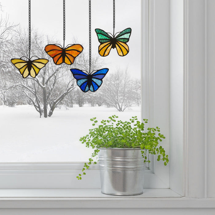 3.2" H Butterfly Kaleidoscope Stained Glass Window Panel Set hanging above a potted plant on a windowsill.