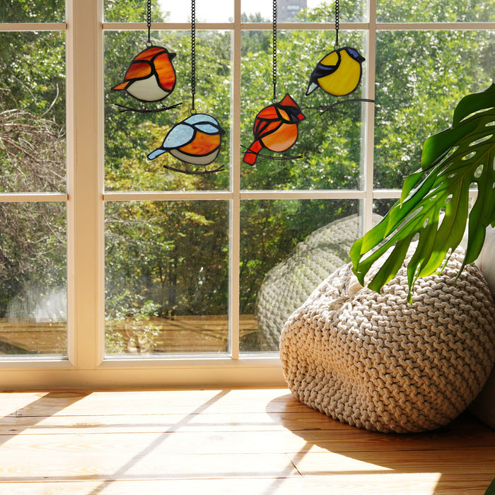 4.5" H Bird Quartet Stained Glass Window Panel Set hanging by a window with a plant in the foreground.