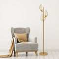 59.25"H Noelle Gold Leaf Shade Floor Lamp next to a gray armchair with beige pillow and blanket on a white background