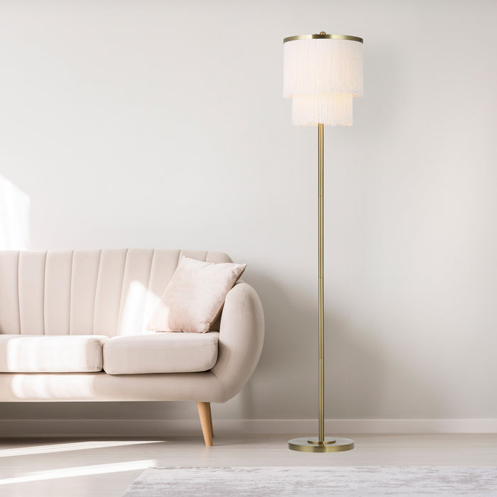 63"H Polished Metal Floor Lamp With Cream Fringe Shade next to a beige sofa in a minimalistic living room.