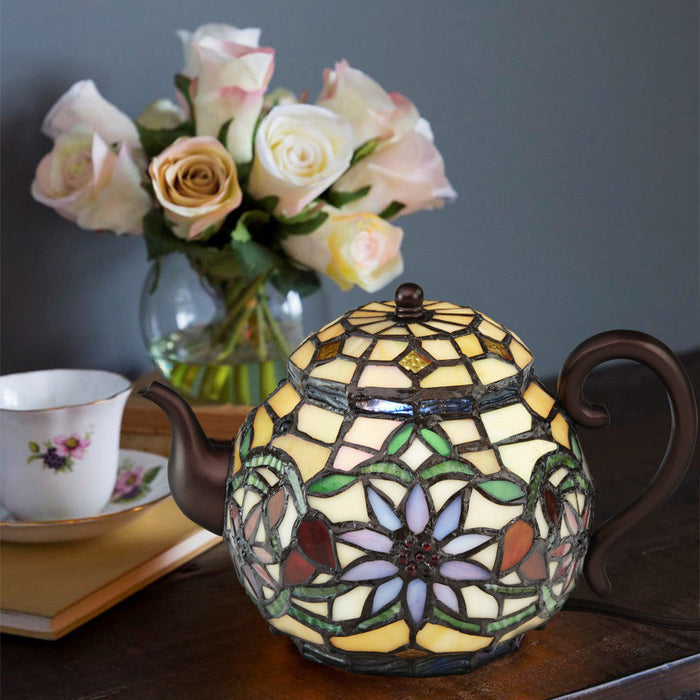 6.5"H Stained Glass Teapot Accent Lamp on a table with flowers and a teacup in the background.