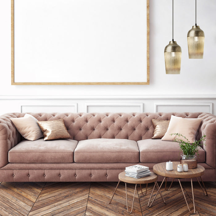 6.8'' W 1-Light Andrea Metal and Glass Pendant hanging above a pink tufted sofa in a living room with wooden floors.