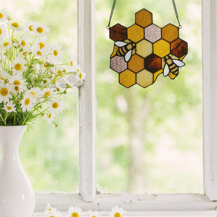 8.25"H Cassie Honeycomb Bees Stained Glass Window Panel hanging on a window, next to a vase of daisies.