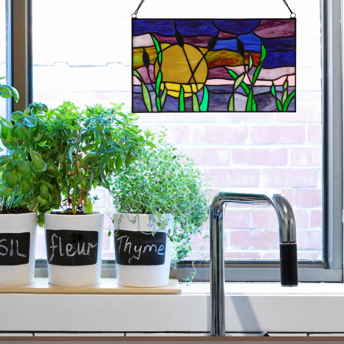 8.25"H Purple Cattails at Sunset Stained Glass Window Panel, hanging on a kitchen window above potted herbs and a faucet.