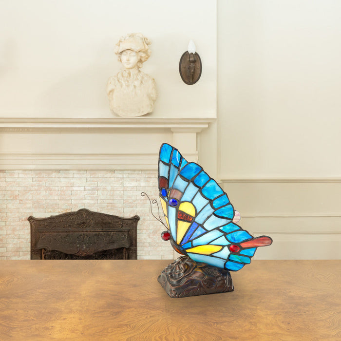 9"H Tiffany Stained Glass Flying Butterfly Accent Lamp on a wooden surface with a fireplace in the background