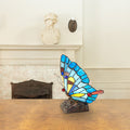 9"H Tiffany Stained Glass Flying Butterfly Accent Lamp on a wooden surface with a fireplace in the background