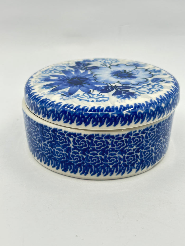 Elevated side view of a round Ceramika Artystyczna Polish pottery trinket box featuring a blue-and-white floral lid and a dense, intricate repeating blue pattern on the base.