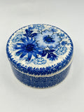 Elevated view of a round Ceramika Artystyczna Polish pottery trinket box featuring a classic blue-and-white floral design on the lid and an intricate repeating blue pattern on the base.
