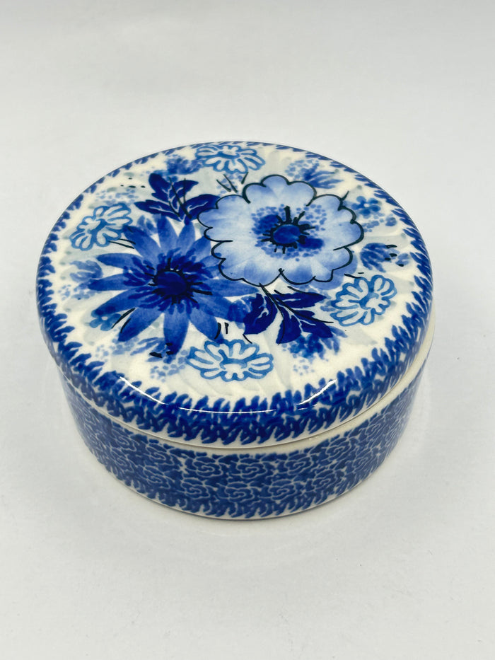 Elevated view of a round Ceramika Artystyczna Polish pottery trinket box featuring a classic blue-and-white floral design on the lid and an intricate repeating blue pattern on the base.