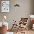 Leslie 11.8" Black Satin Painted Cone-Shaped Pendant Lamp in a modern living room with wooden armchair, decorative vases, and abstract art on the wall.