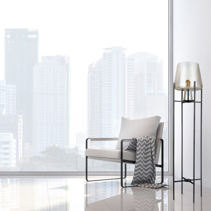 Leticia Black Metal and Champagne Gold Glass Bowl 61-Inch Floor Lamp next to a modern chair with a pillow in a room with large windows showing cityscape.