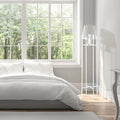 Leticia White Metal and Clear Glass Bowl 61-Inch Floor Lamp in a modern bedroom with white bedding and large windows showing greenery outside.