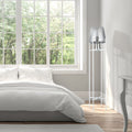 Leticia White Metal and Silver Glass Bowl 61-Inch Floor Lamp next to a neatly made bed in a bright bedroom with large windows.