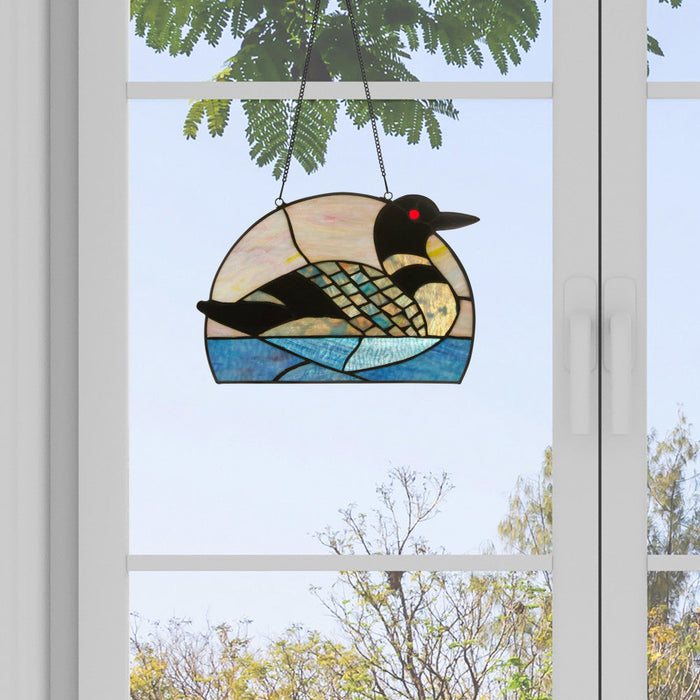Loon Stained Glass Window Panel hanging in front of a window with a view of trees.