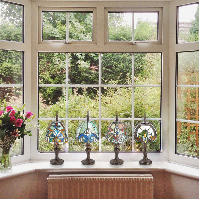 Set of 4 Family Favorites Tiffany Style Stained Glass Mini Accent Lamps on a windowsill with a view of greenery outside.